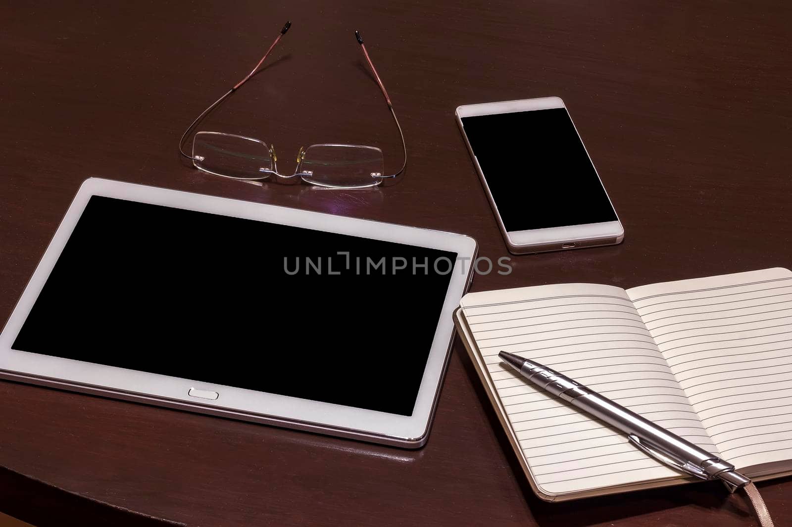 Office table: mobile phone, tablet, glasses, notebook and pen with copy space. Gadgets on a wooden table