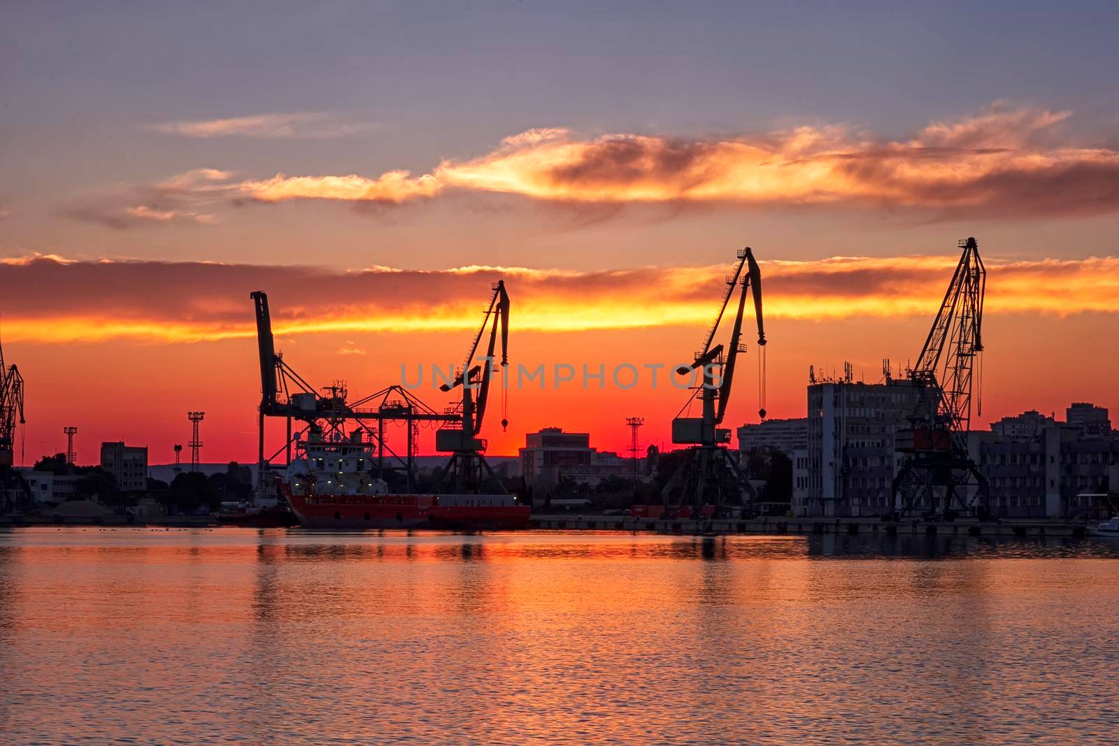 Silhouettes of port cranes at stunning red sunset. Cargo ship terminal at the twilight scene.