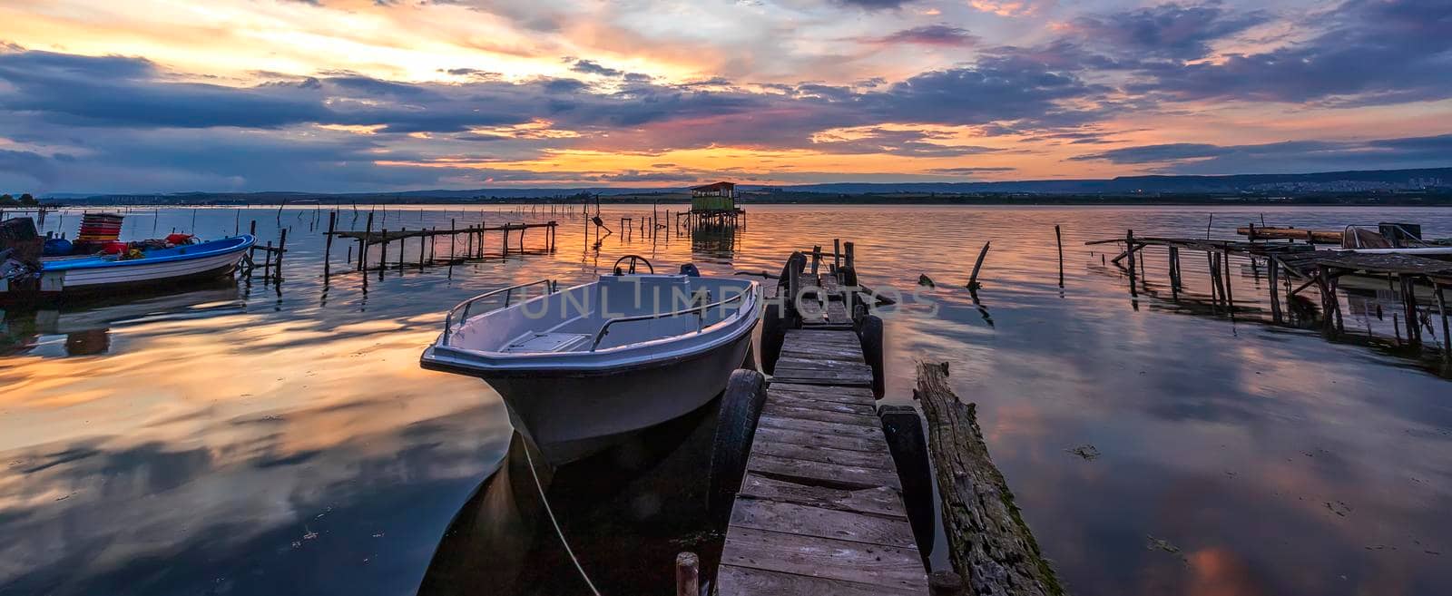 Amazing mood sunset at a lake coast with a boat at a wooden pier. by EdVal