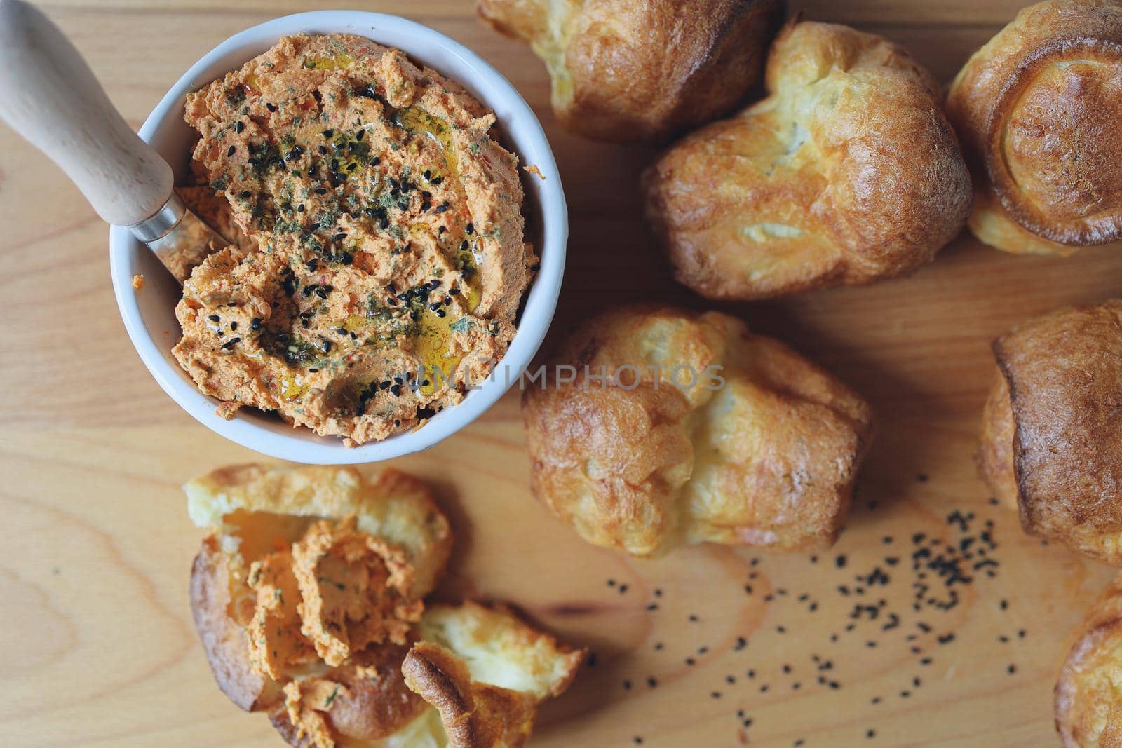 ricotta dip with sun-dried tomatoes and baked paprika in a ceramic white bowl and homemade popovers, which is a puffed, airy, and eggy hollow roll, is fresh from the oven. Top View