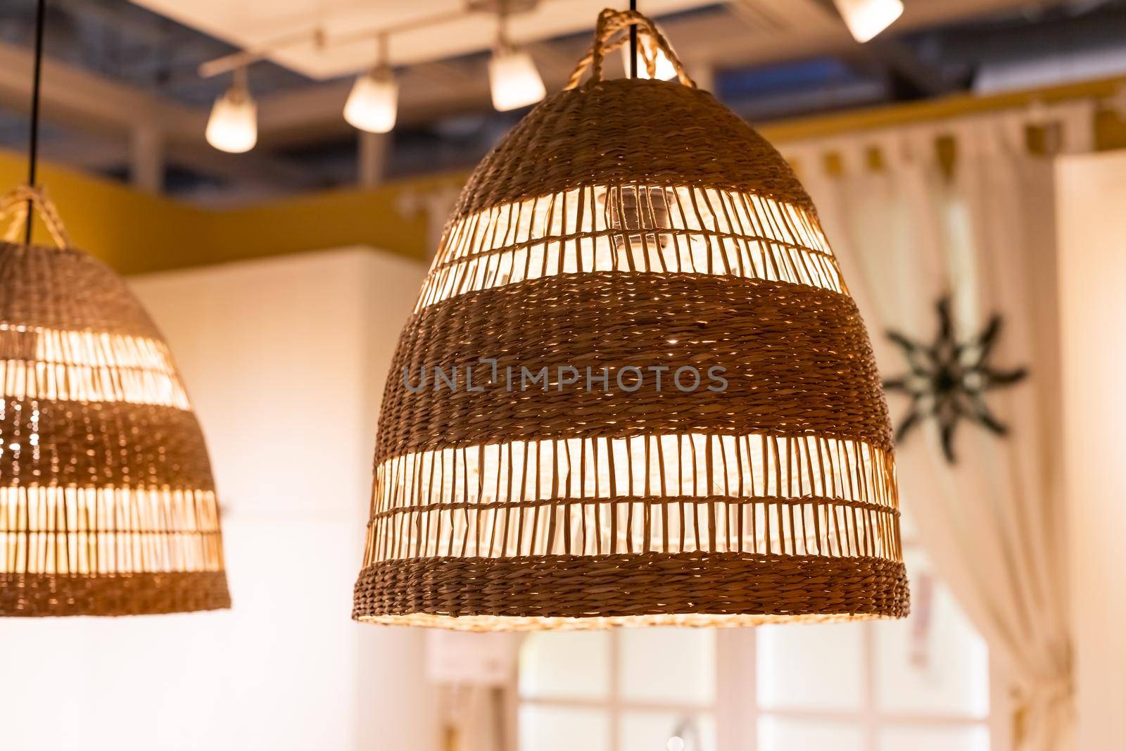 A stylish wicker wooden chandelier in boho and Bali style hangs on the ceiling near a white canopy made of weightless tulle.