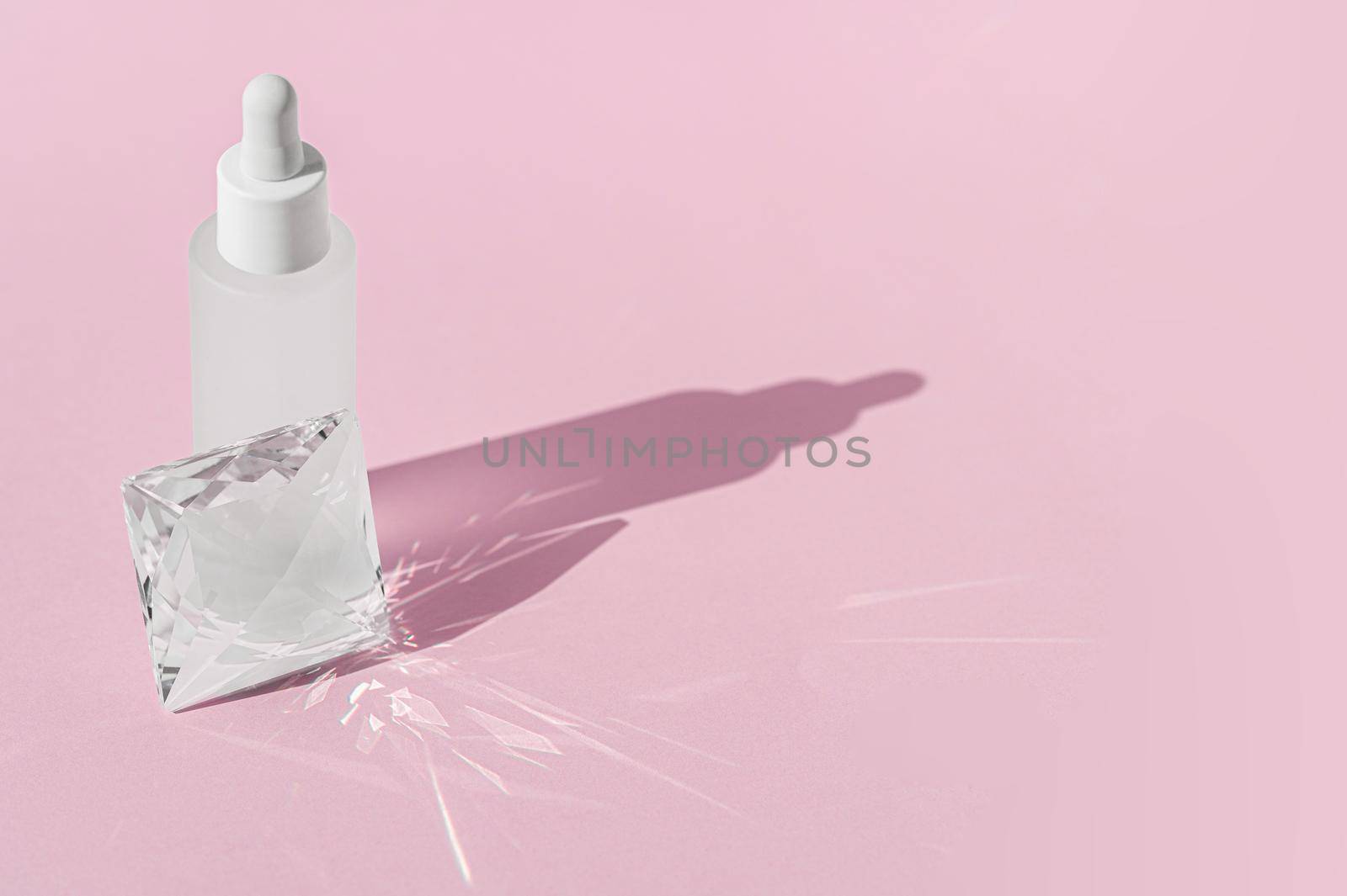 Serum cosmetic bottle mockup with quartz transparent prism crystal on pink background, with glass prism refracting light effects and rays of light. Product presentation..