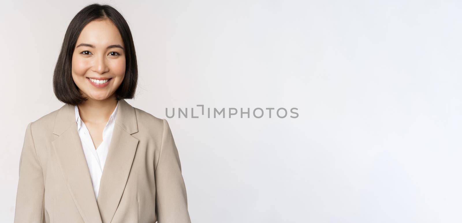 Portrait of successful businesswoman in suit, smiling and looking like professional at camera, white background.