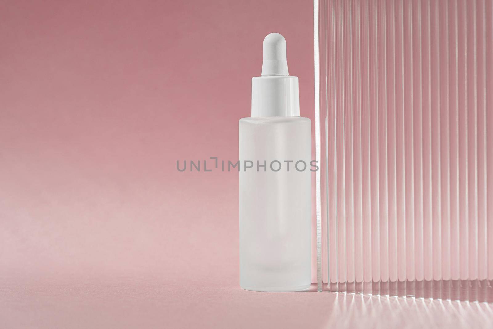 Transparent liquid product in glass bottle. Anti aging serum with collagen and peptides on pink surface with acrylic ribbed waved sheet. Hyaluronic acid oil mockup. Beauty product mock up. Banner