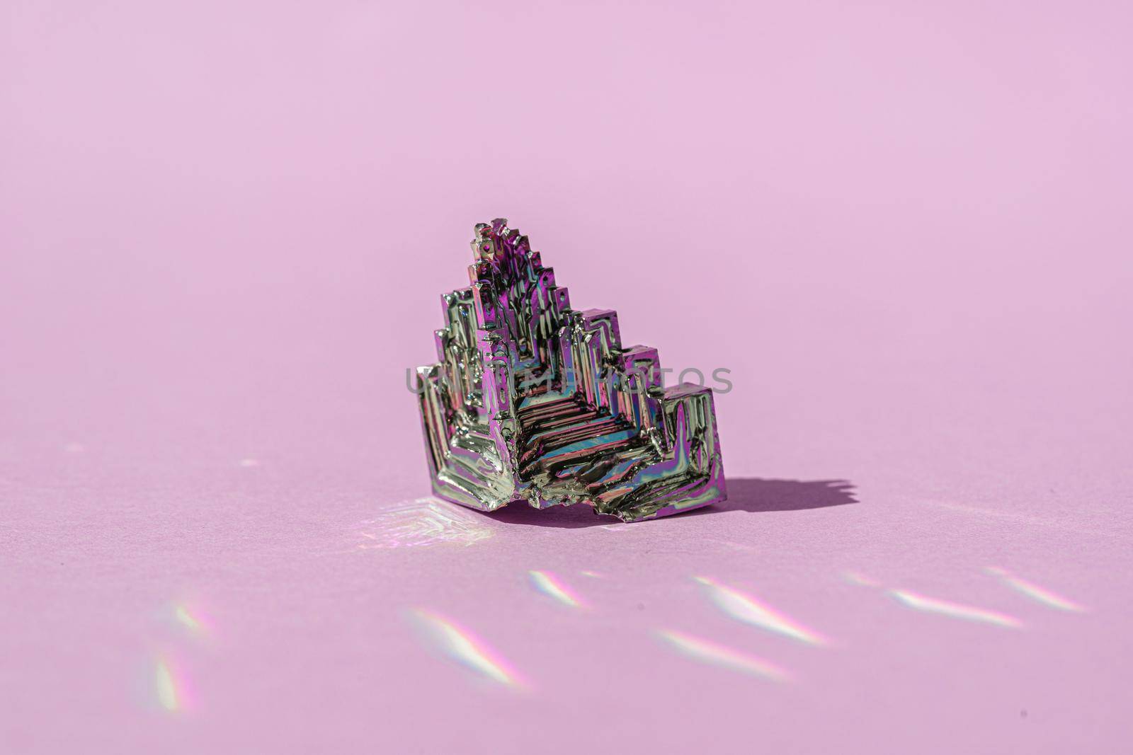 Synthetic bismuth Bismuthum crystal with iridescent oxide film on pink background close up isolated. Amazing colorful shiny rainbow Bismuth Gemstone mineral. by photolime