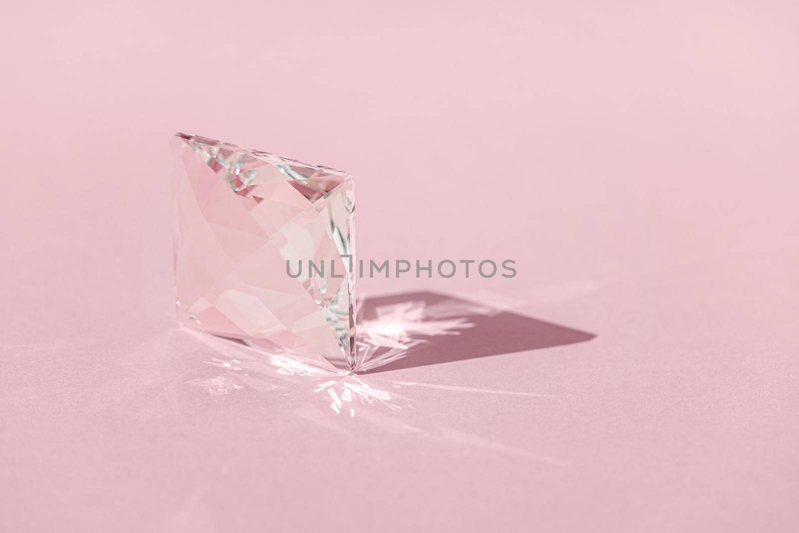 Crystal prism with light diffraction of spectrum colours and reflection with trendy light and hard shadows on pink background. Light spectrum reflected through glass prism. Banner