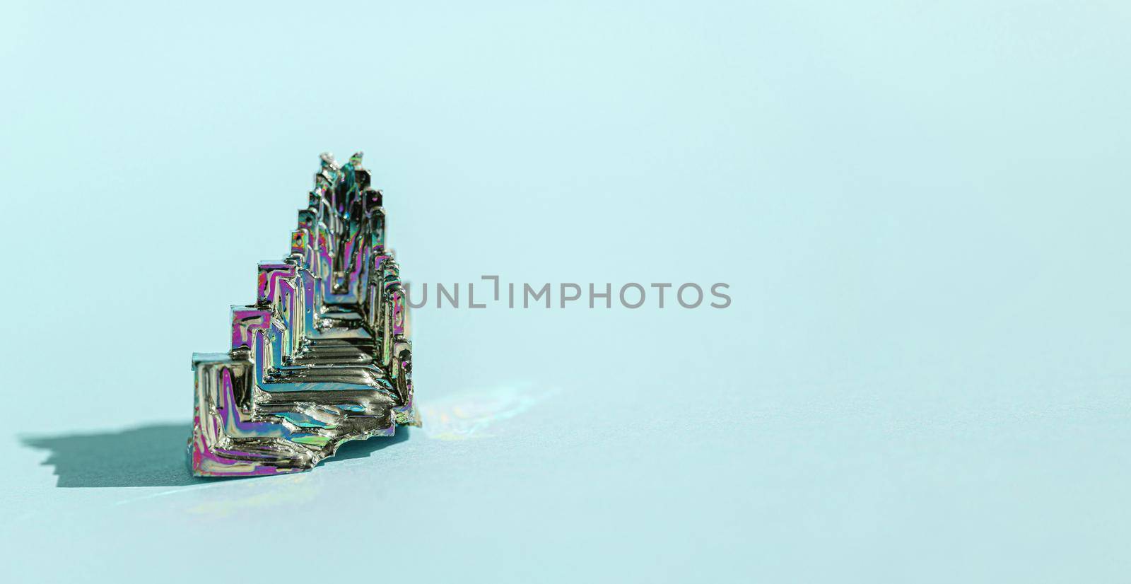 Synthetic bismuth Bismuthum crystal with iridescent oxide film on blue background close up isolated. Amazing colorful shiny rainbow Bismuth Gemstone mineral. Banner