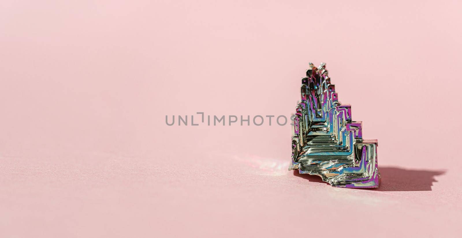 Synthetic bismuth Bismuthumcrystal with iridescent oxide film on pink background close up isolated. Amazing colorful shiny rainbow Bismuth Gemstone mineral by photolime