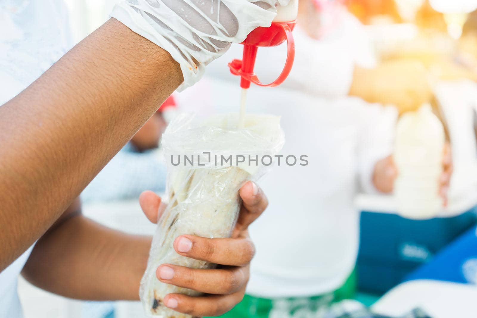 Closeup of the hands of a Nicaraguan woman putting sour cream from a jar onto a traditional dish called quesillo tucked in a plastic bag, a thin sheet of artisanal mozarella cheese on a corn tortilla