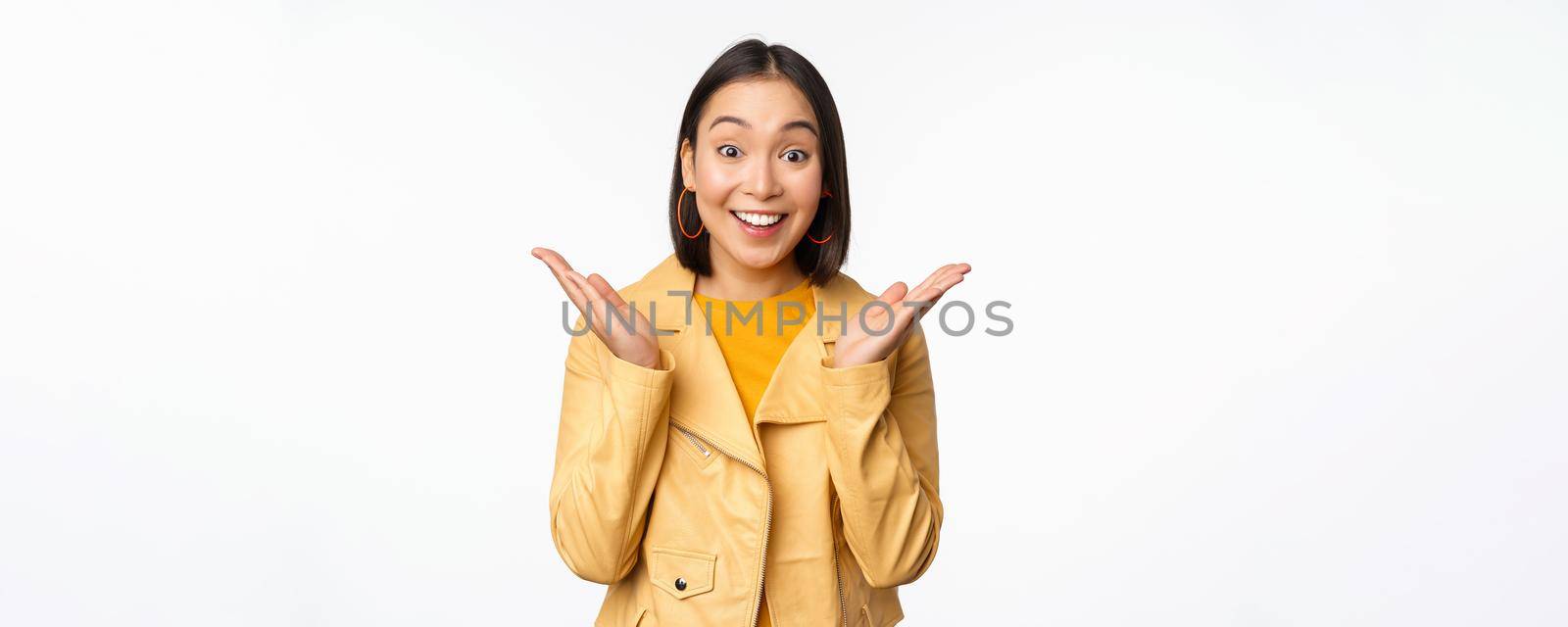 Image of asian woman looking surprised, amazed reaction, shocked face, standing over white background. Copy space