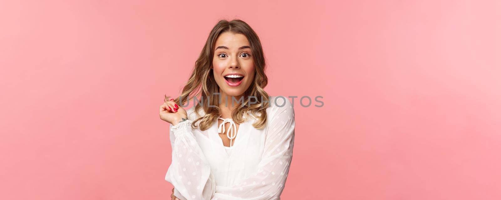 Surprised and amazed good-looking blond girl listening with interest to girlfriend story while attend beauty salon, rolling hair strand on finger and look astonished camera with pleased smile.