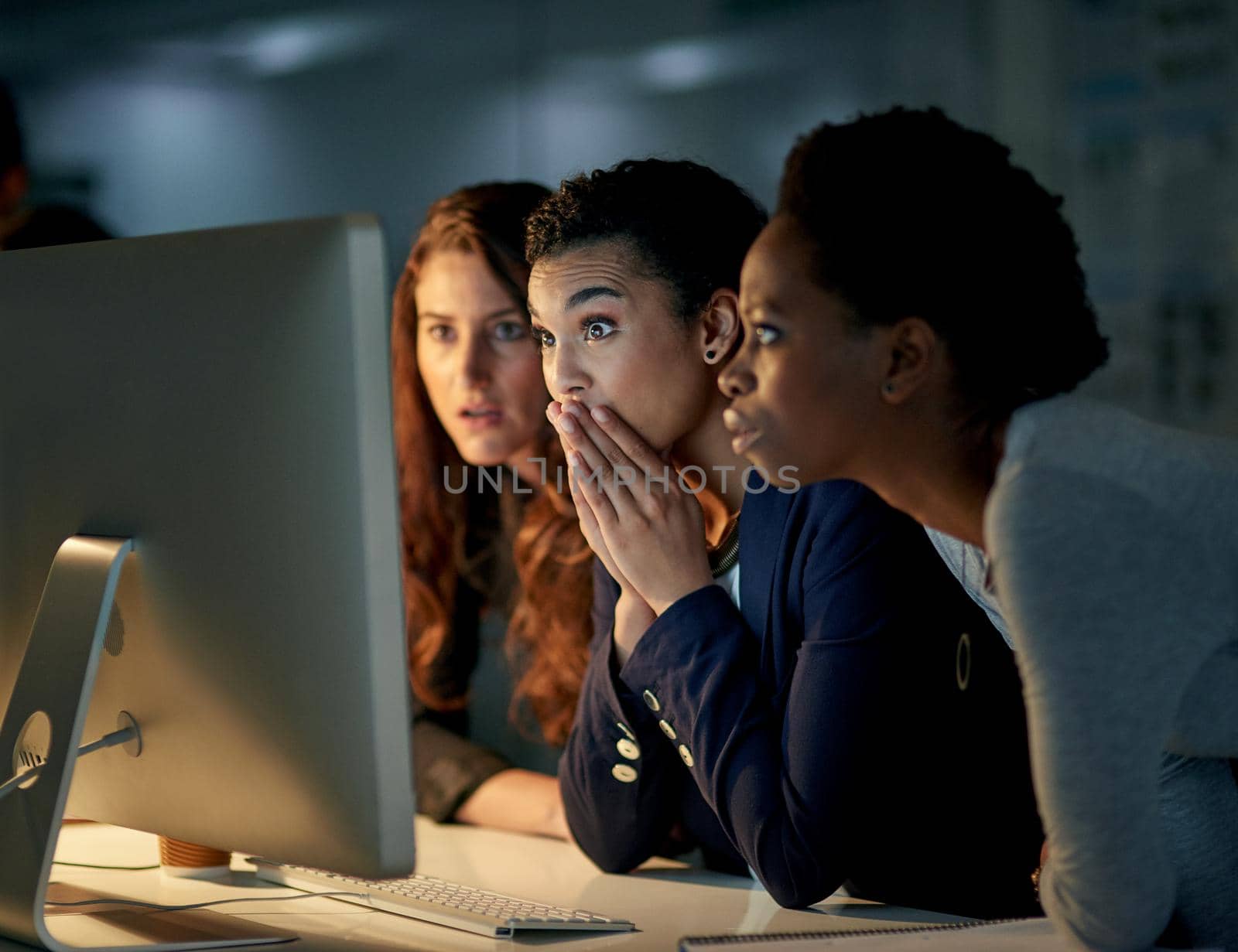 Cropped shot of a group of colleagues looking shocked while working late in an office.