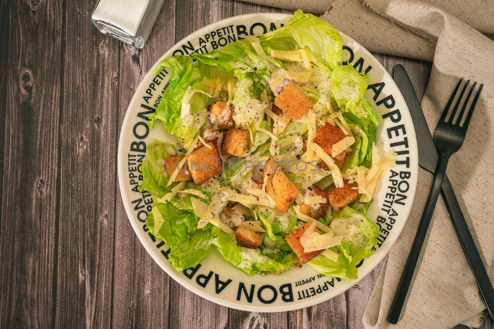 Exquisite traditional Caesar salad of lettuce, toasted bread and fine Parmesan cheese with a garlic aioli and olive oil in a bowl that says Bon Appetite in French. Top view.