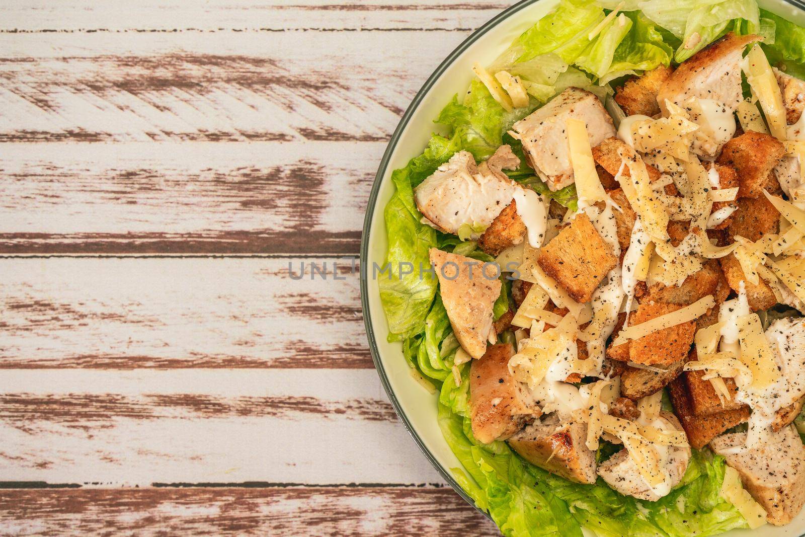 Exquisite Caesar salad with small bites of chicken and a traditional aioli sauce in a small bowl on a rustic table. Top view. Close-up detail. Large Copy space.