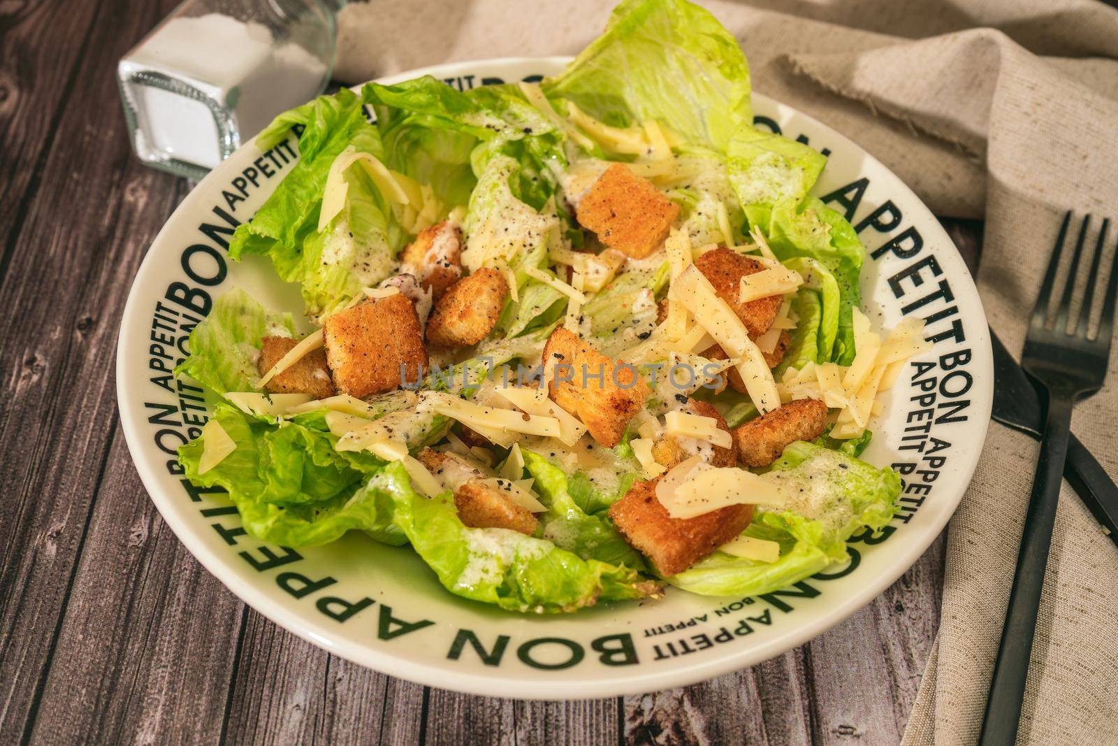 Exquisite traditional Caesar salad of lettuce, toasted bread and fine Parmesan cheese with a garlic aioli and olive oil in a bowl that says Bon Appetite in French. View at 45 degrees.