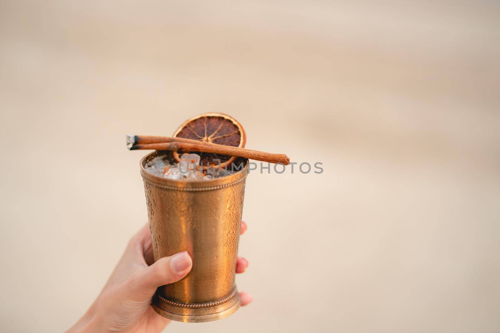 Hand with cocktail, Alcoholic drink with ice, orange and cinnamon on the beach.