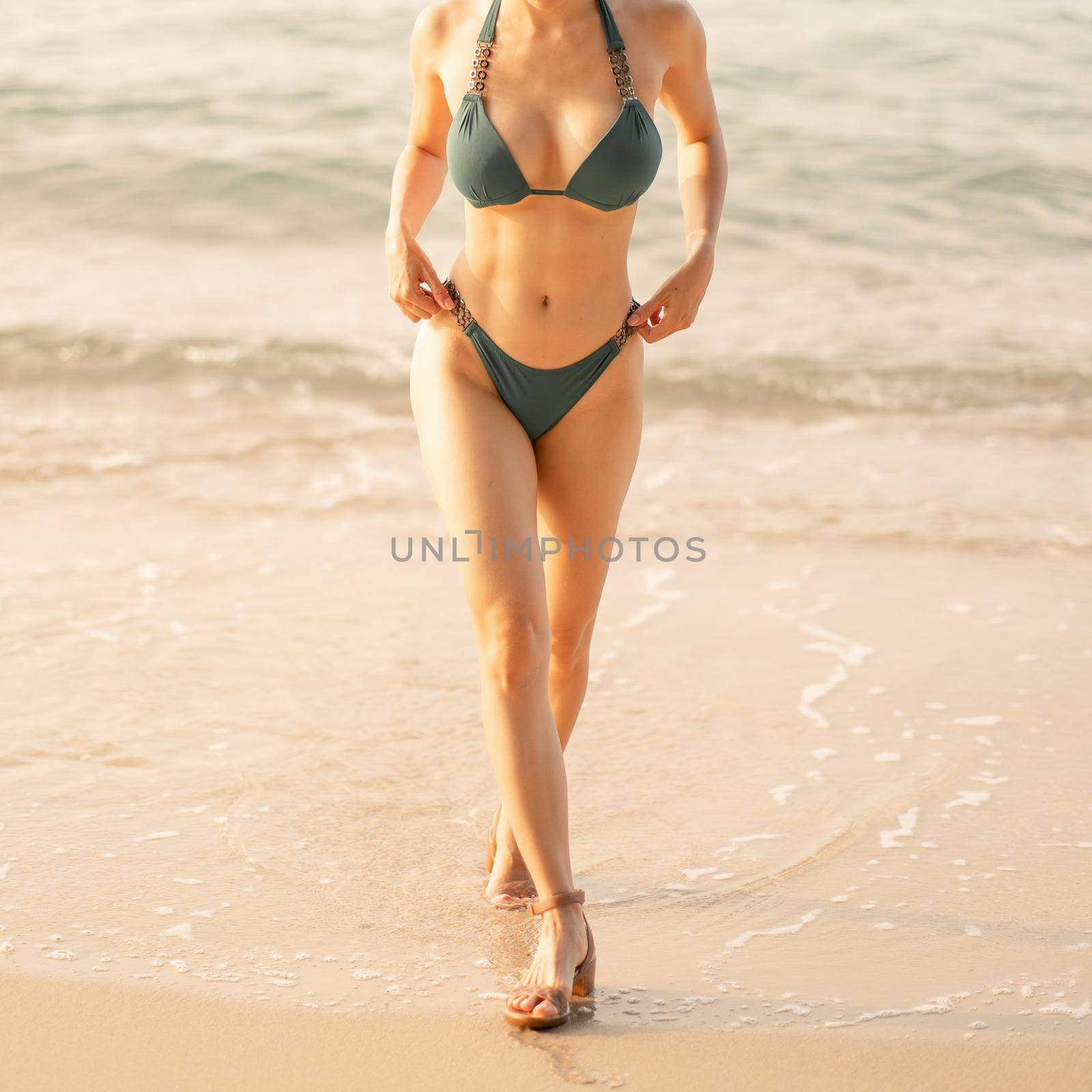 Close up of woman body in green bikini walking on beach.