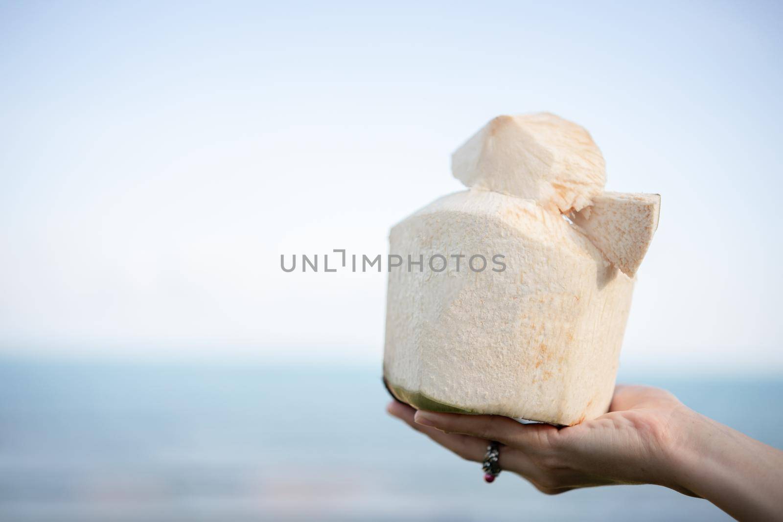 Fresh coconut cocktail in hand over ocean background.
