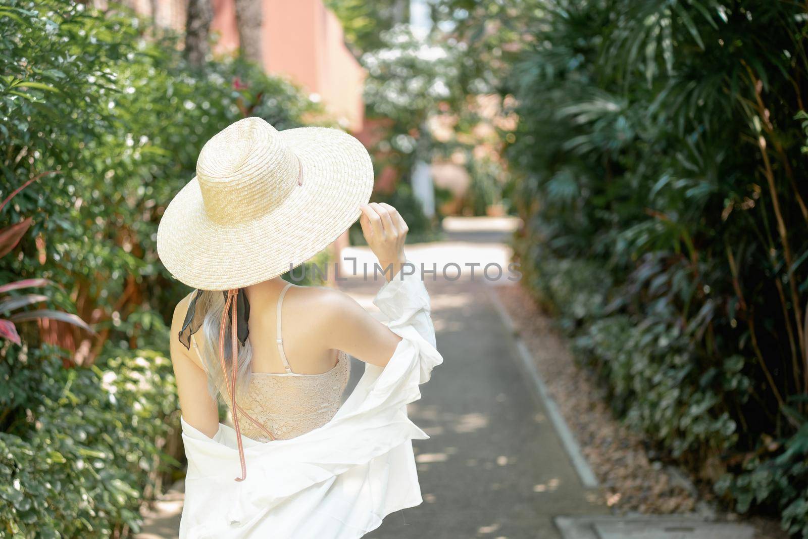 Back view of woman wearing white shirt, long skirt and straw hat posing tropical garden. by sirawit99