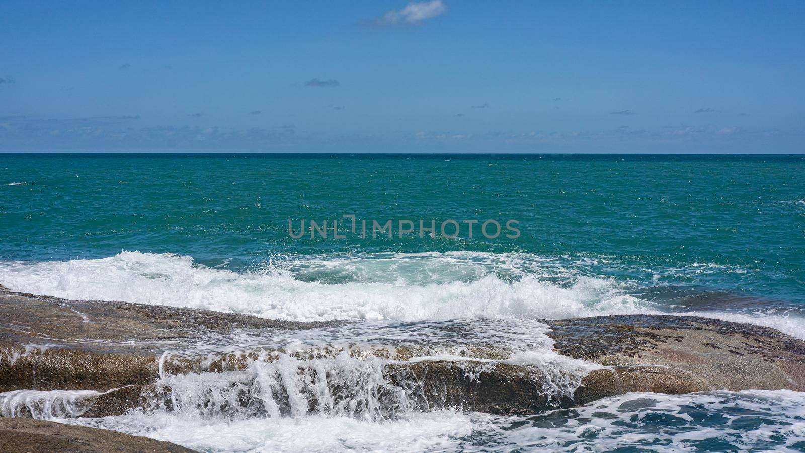 Rocky beach with white waves, deep blue ocean views and blue sky.