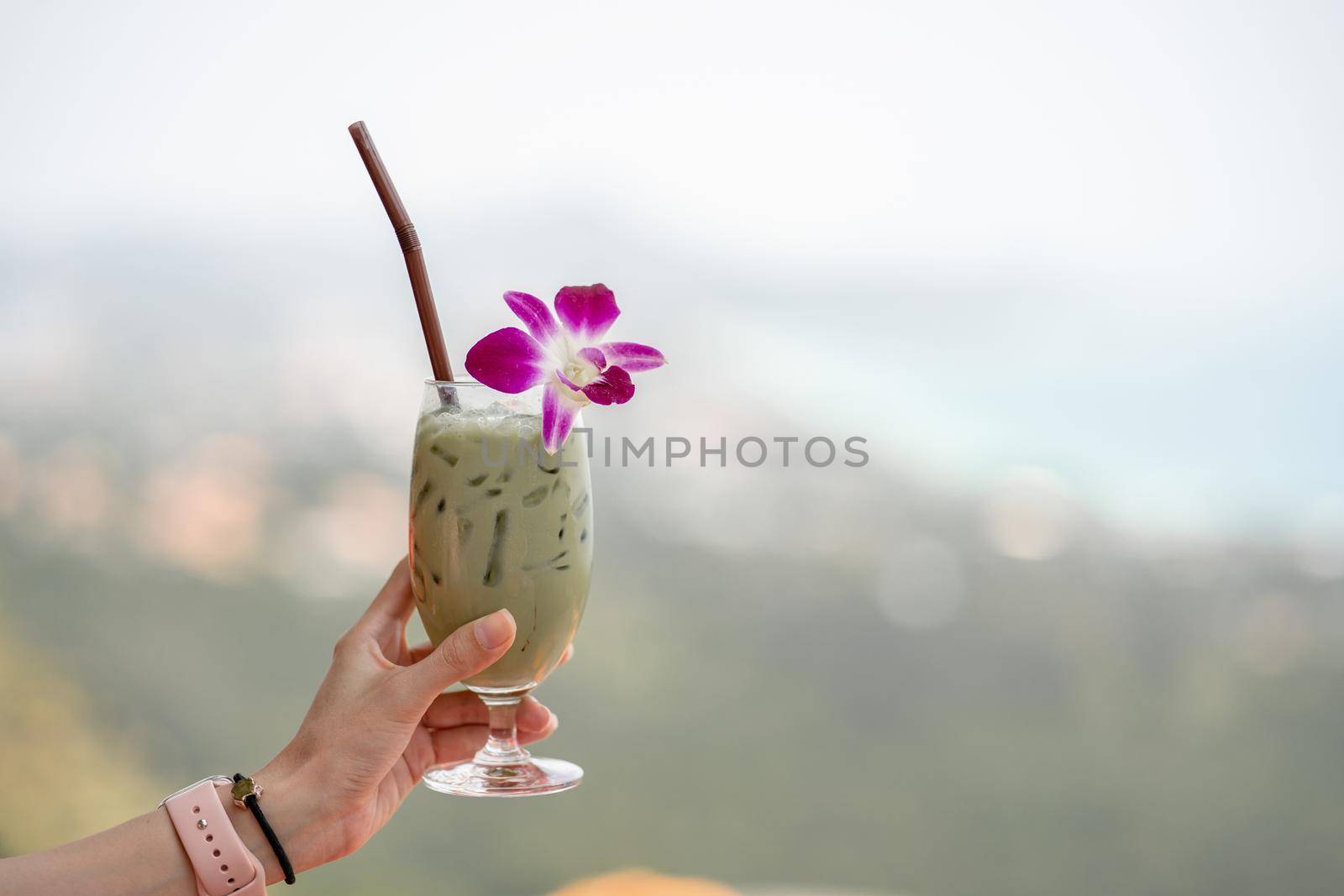 Hand holding green tea matcha latte cold beverage drink with orchid flower.