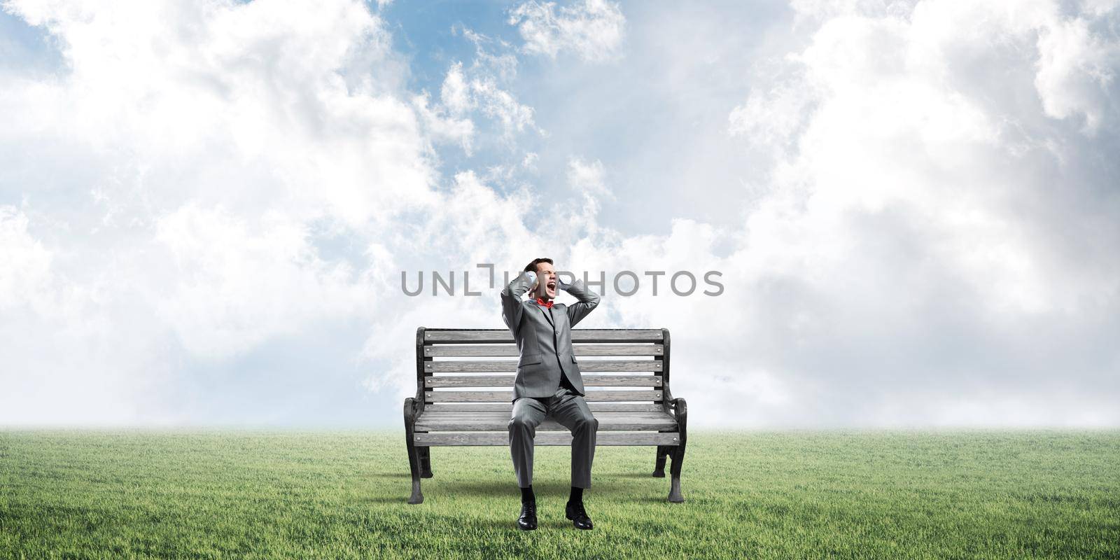 Frustrated businessman sitting on bench and closing ears with hands