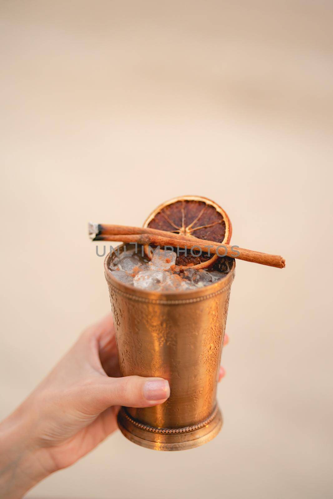 Hand with cocktail, Alcoholic drink with ice, orange and cinnamon on the beach.