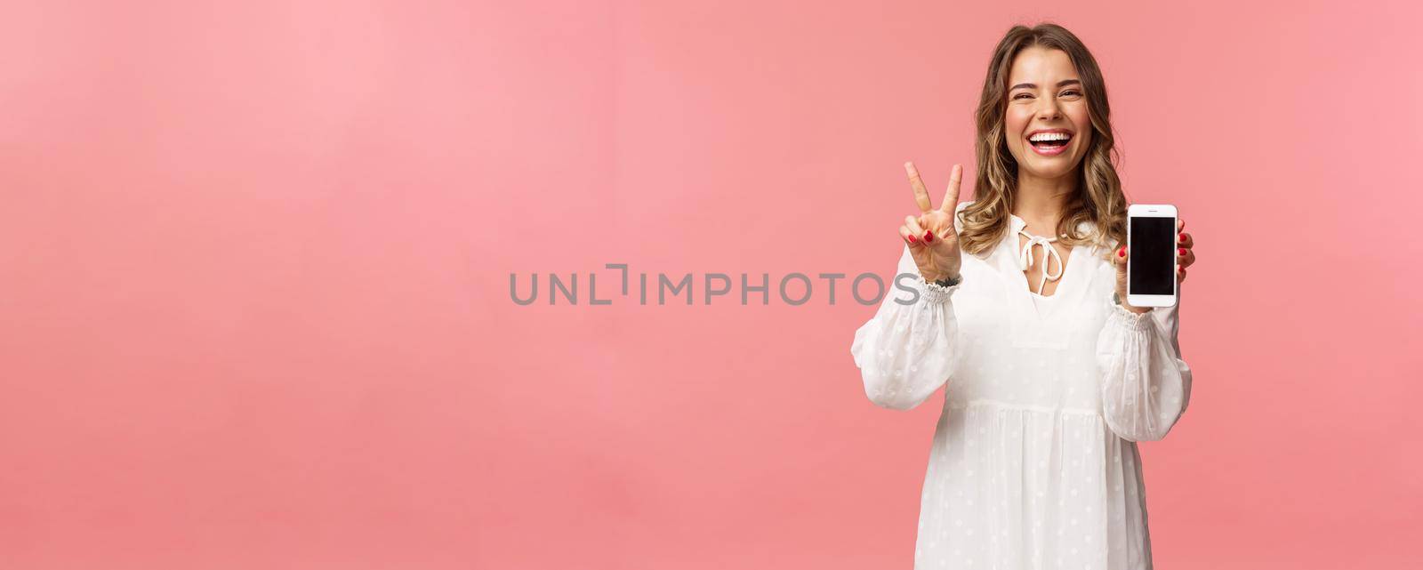 Portrait of kawaii optimistic and happy young girl in white dress, show mobile phone display and peace sign, laughing feeling cheerful and glad to share awesome app, useful link, pink background by Benzoix