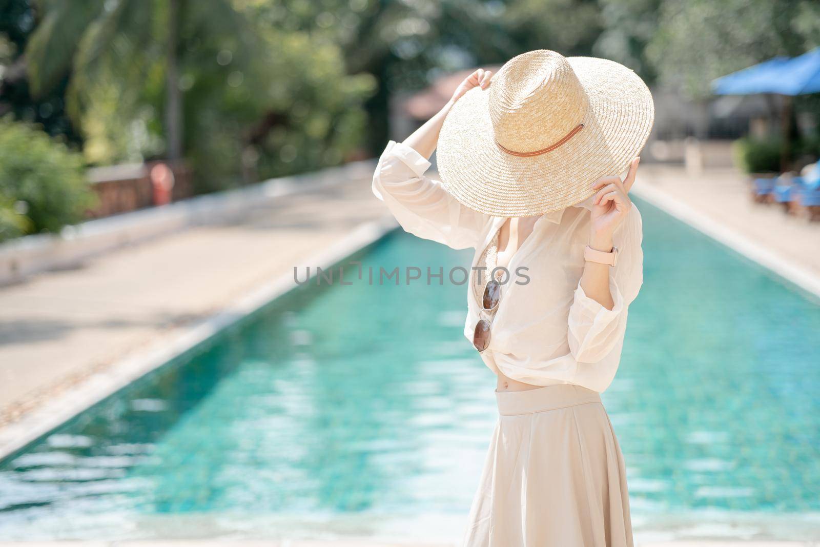 Woman wearing white shirt, long skirt and straw hat posing near swimming pool. by sirawit99