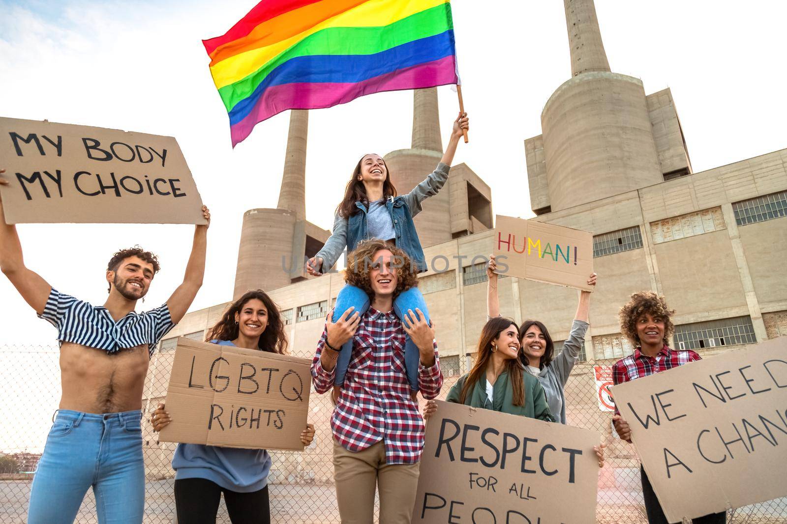 Multiracial protesters demonstrate for LGTB rights holdings placards and waving rainbow flag. by Hoverstock