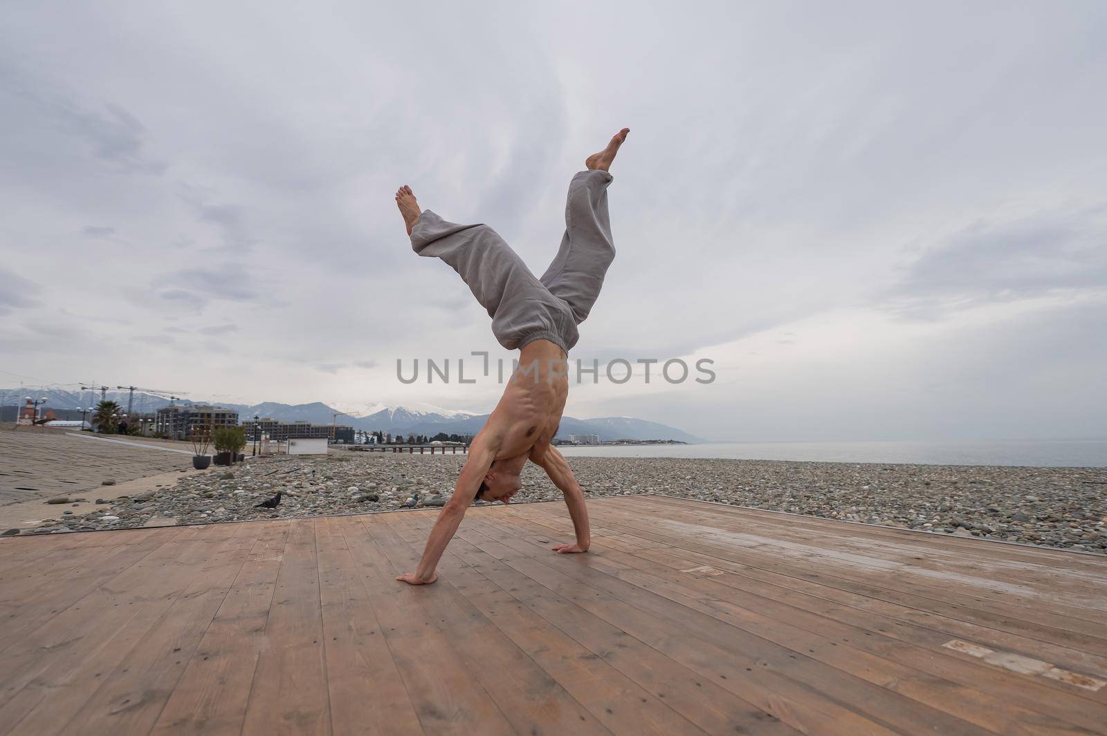 Shirtless caucasian man doing backflip on pebble beach