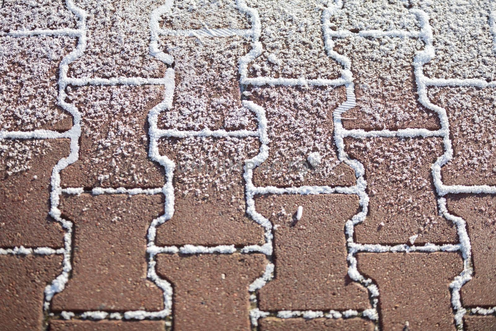 Close-up frame of a red paving stone that is partially covered with white fresh snow.