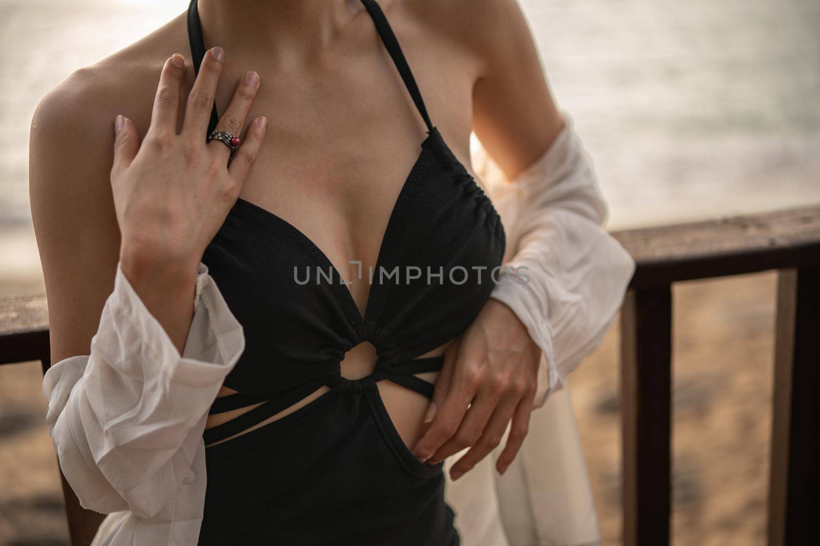 Close up of woman in black dress standing on a balcony, ocean view.