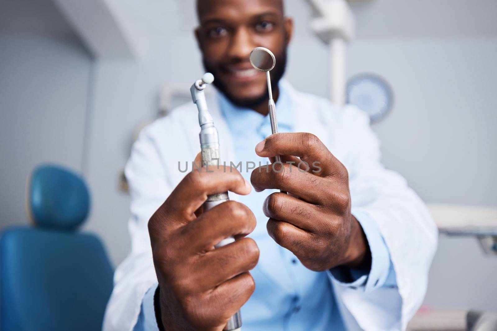 Portrait of a young man holding teeth cleaning tools in his dentists office.