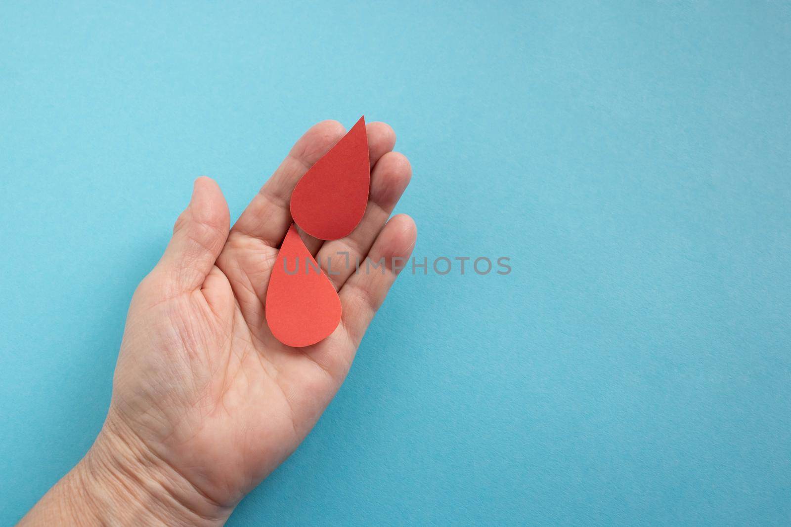 The concept of the World Blood Donor and Hemophilia Day. Two red paper drops of blood in the hand on a blue background.