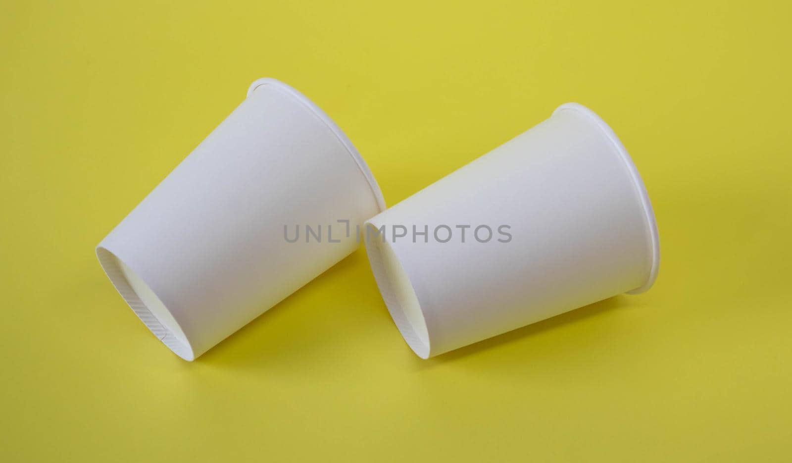Two small white paper cups on a yellow background by lapushka62
