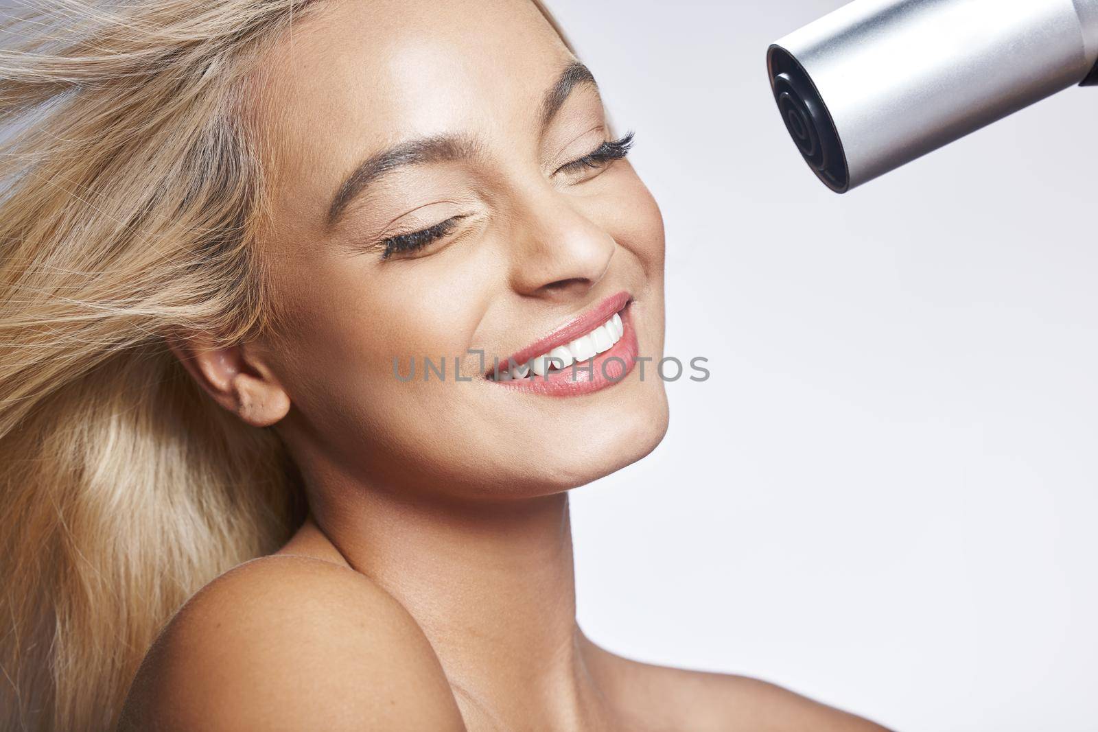 Shot of an attractive young woman standing alone against a grey background in the studio and using a hairdryer.