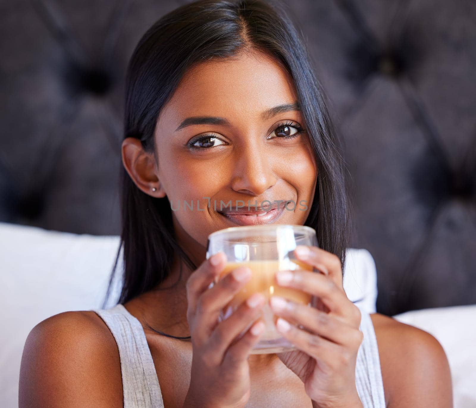 Shot of a young woman drinking a hot beverage while sitting on her bed.