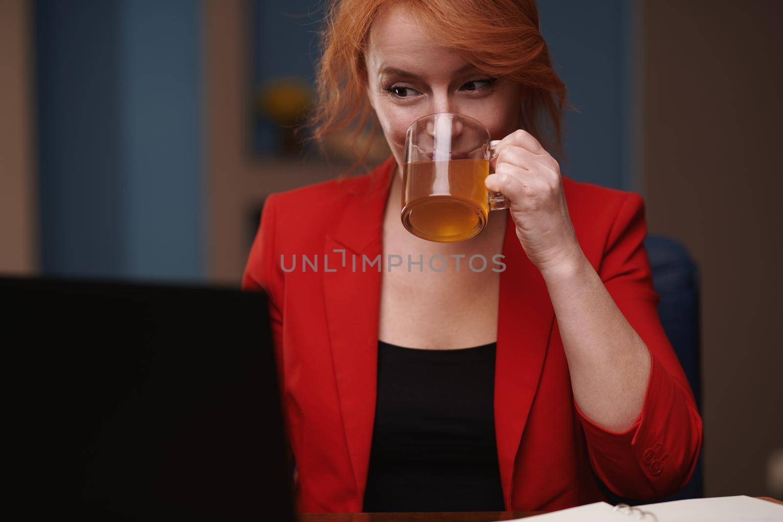 Businesswoman drinking tea while working on laptop at the office by Novic