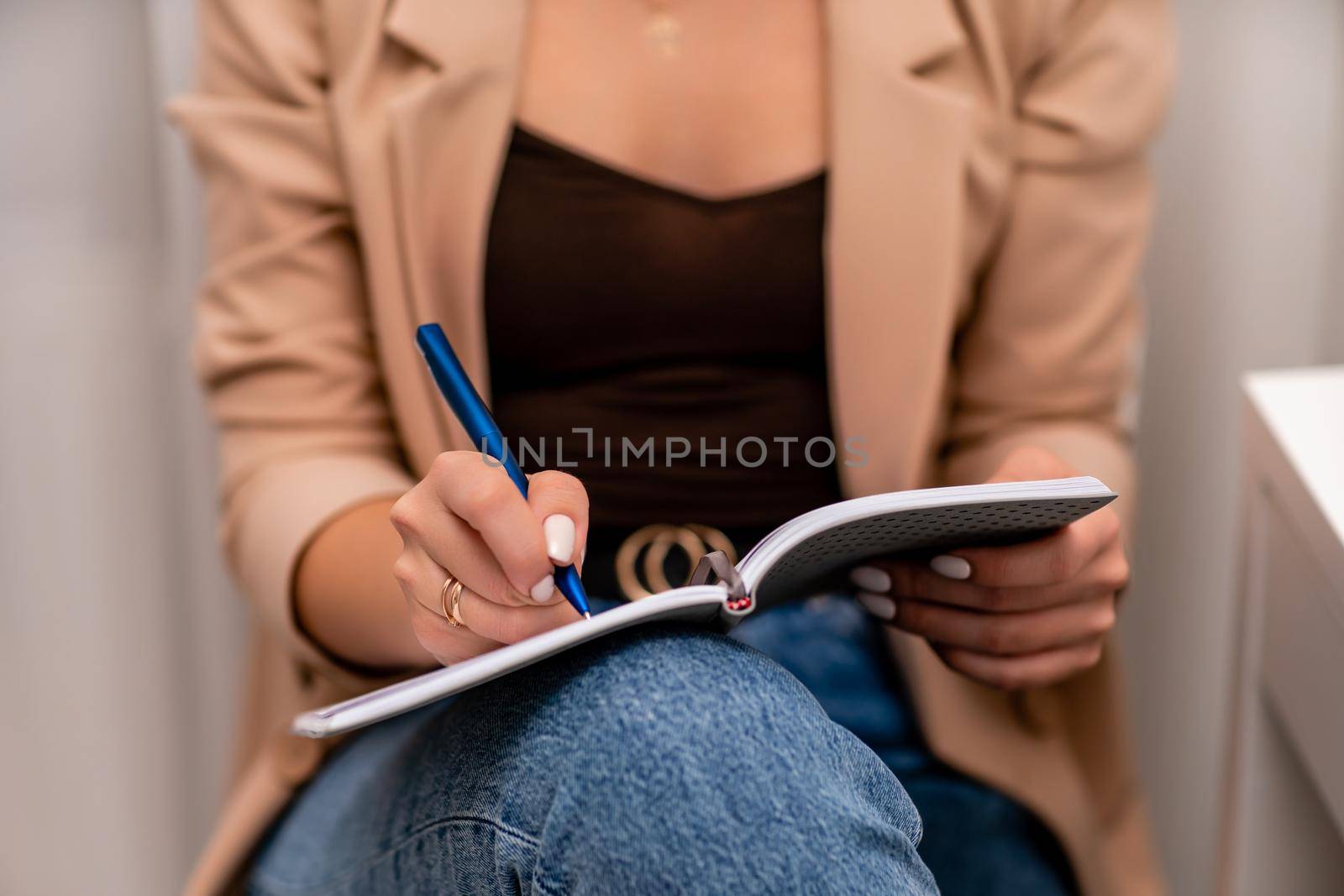 European woman writes in a notebook. She is wearing a beige jacket and jeans