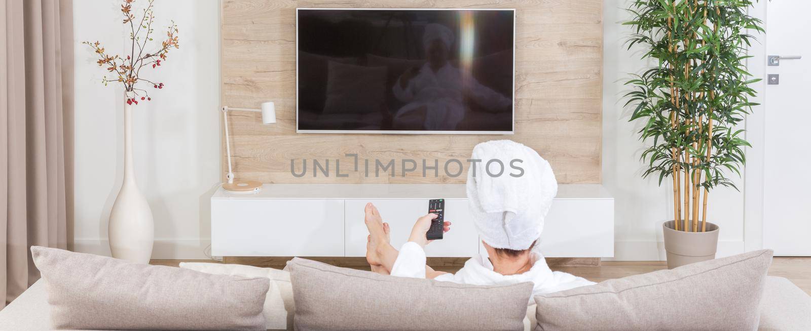 Woman sitting on couch with towel on her head watching tv