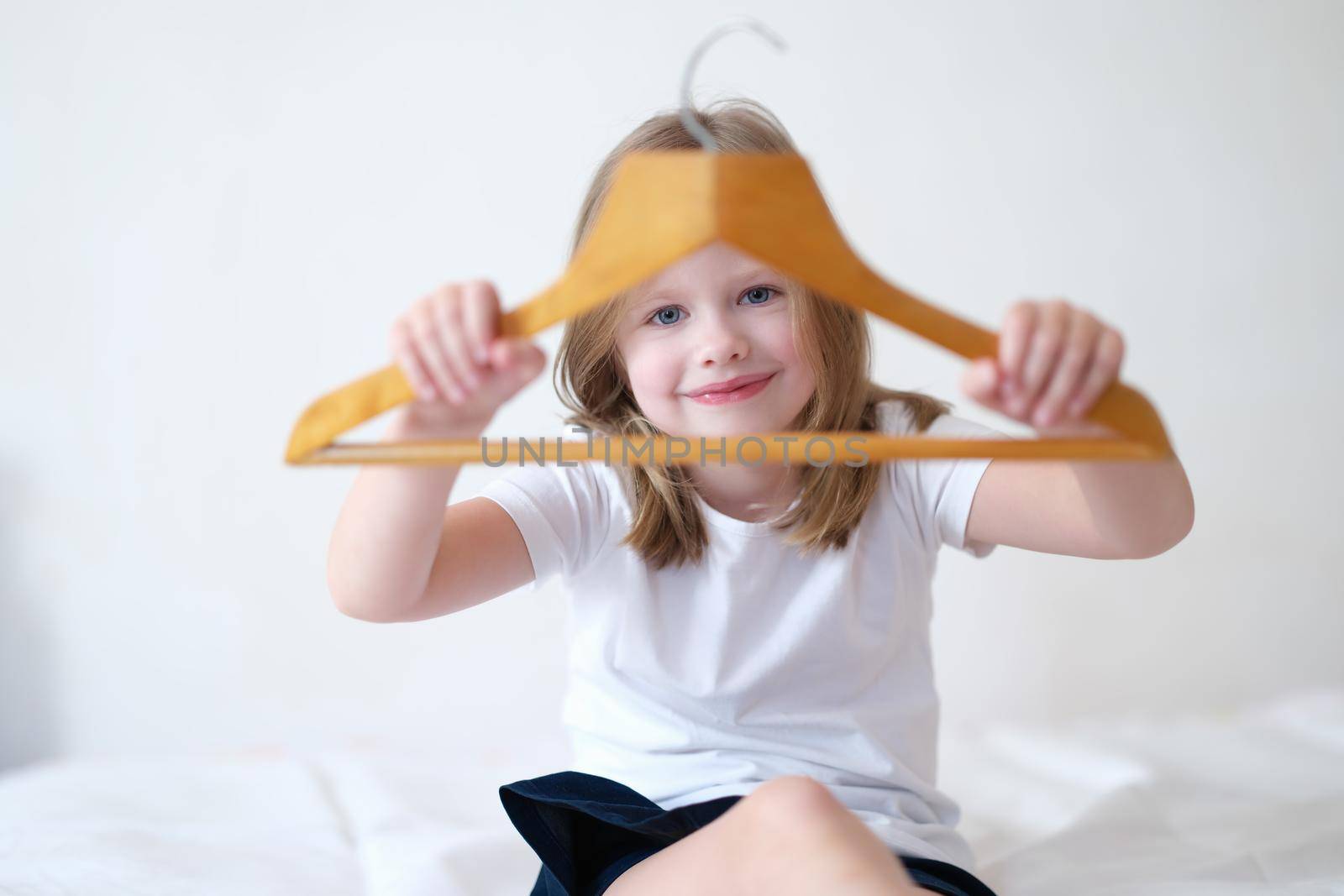 Little girl holding wooden clothes hanger in hands. Children online shopping concept