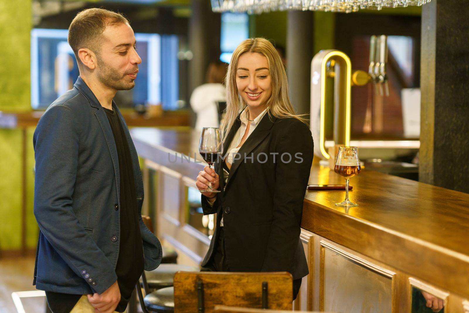 Cheerful multiracial man and woman with alcohol drinks smiling and looking at each other while having date in bar