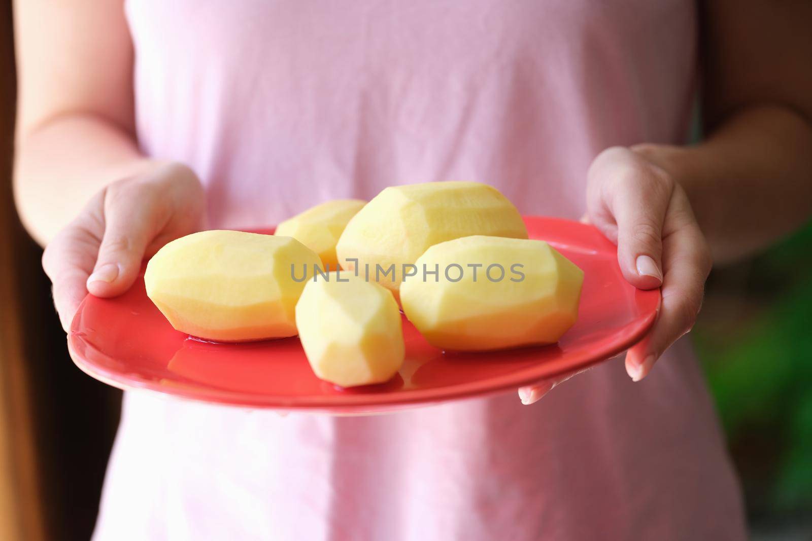 Woman housewife holding plate of peeled potatoes in her hands closeup. Potato recipes concept