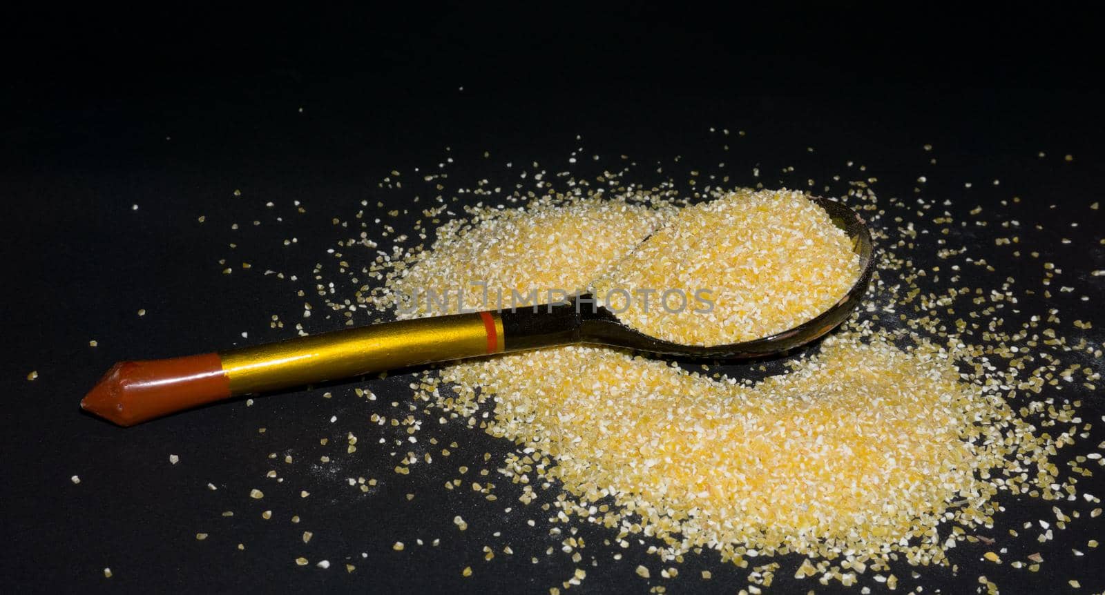 Raw bright yellow corn grits flour in a Khokhloma spoon and grains are scattered around.