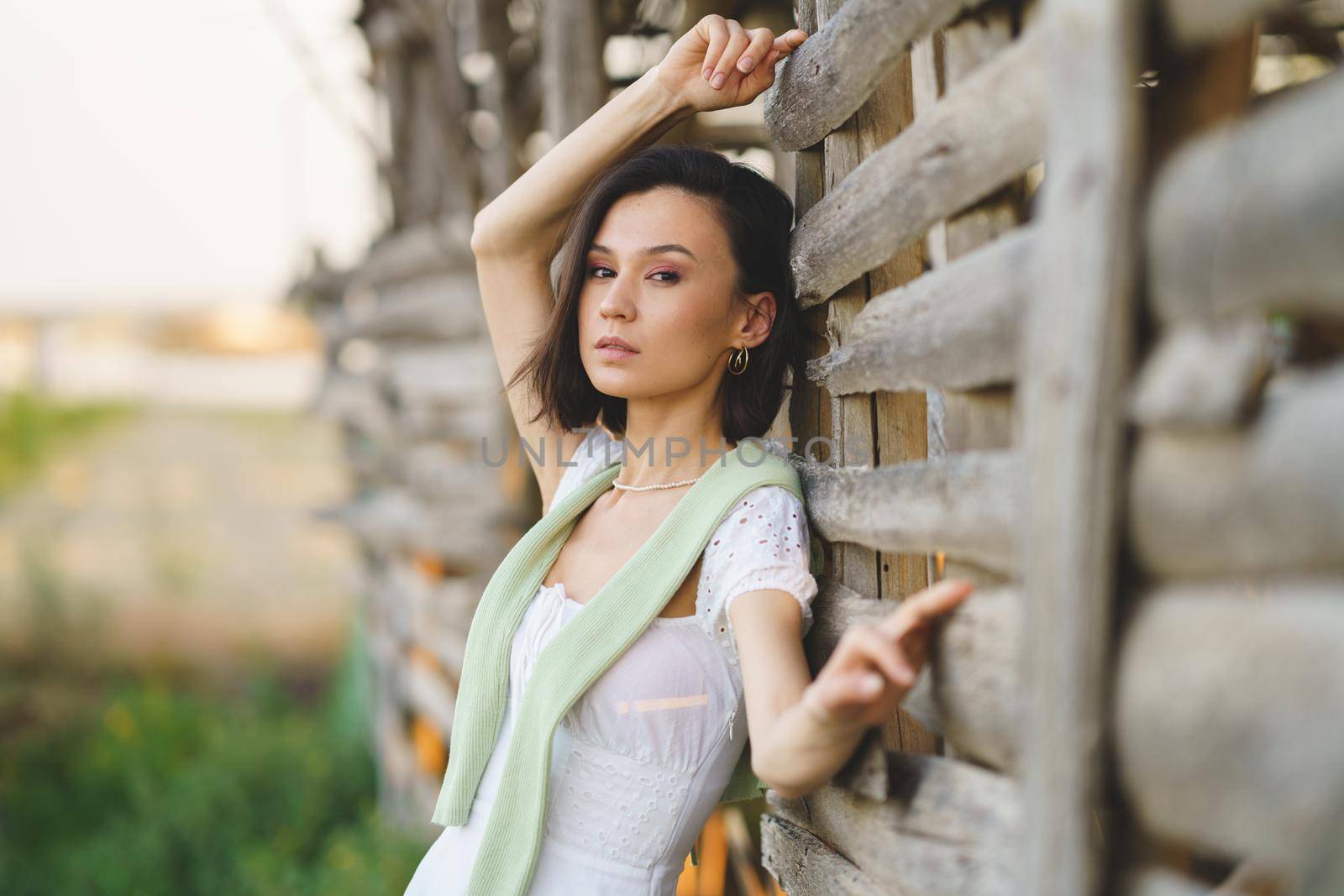 Pretty young Asian woman, posing near a tobacco drying shed, wearing a white dress and green wellies. Beauty and fashion concept