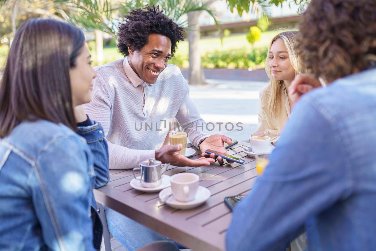 Company of positive diverse friends sitting at table in summer cafe and enjoying meeting while looking at each other