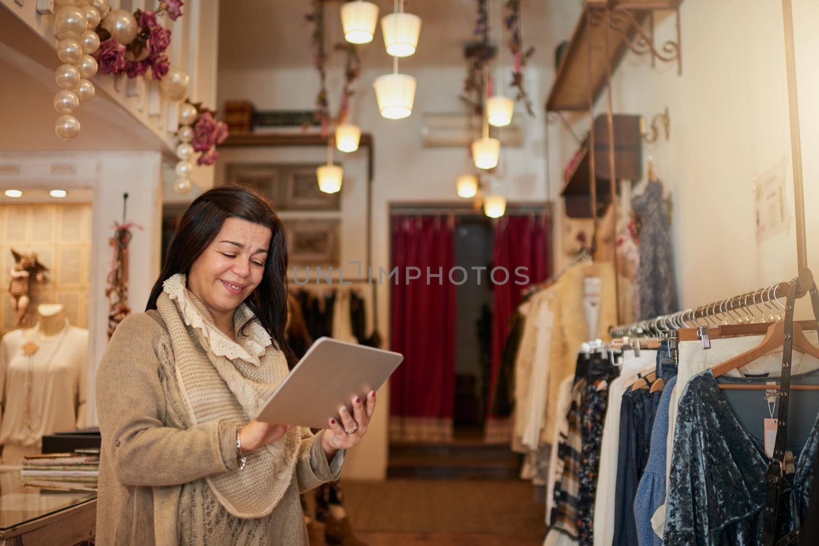 Technology is a business best friend. Cropped shot of an attractive mature female entrepreneur working on a tablet in her self-owned boutique. by YuriArcurs