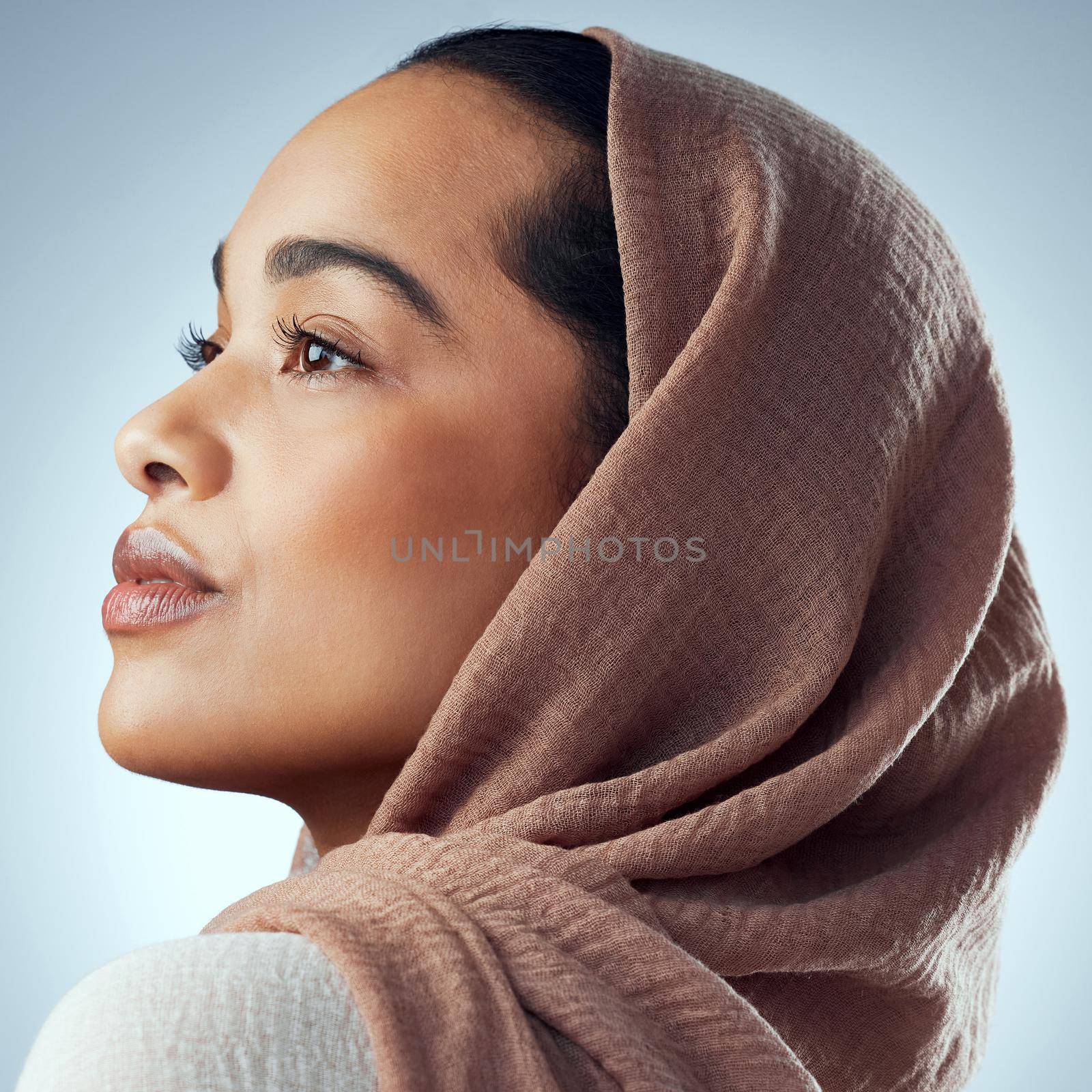 Studio shot of a beautiful young woman wearing a headscarf against a grey background.