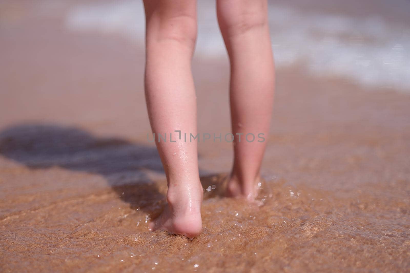 Bare feet of child walking along sea shore closeup. Holidays at resort with children concept